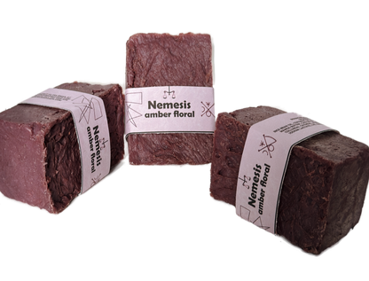 Three Nemesis soap bars arranged in a triangular grouping on a white background, showing the rich maroon color and lavender label from multiple angles
