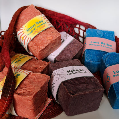 Assorted Bouncing Studio bars displayed in a crimson knit mesh bag: Shiny Boy (coral), Nemesis (maroon), and Love Potion (blue) bars visible with their branded labels